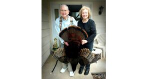 An old couple holding up a turkey on their porch