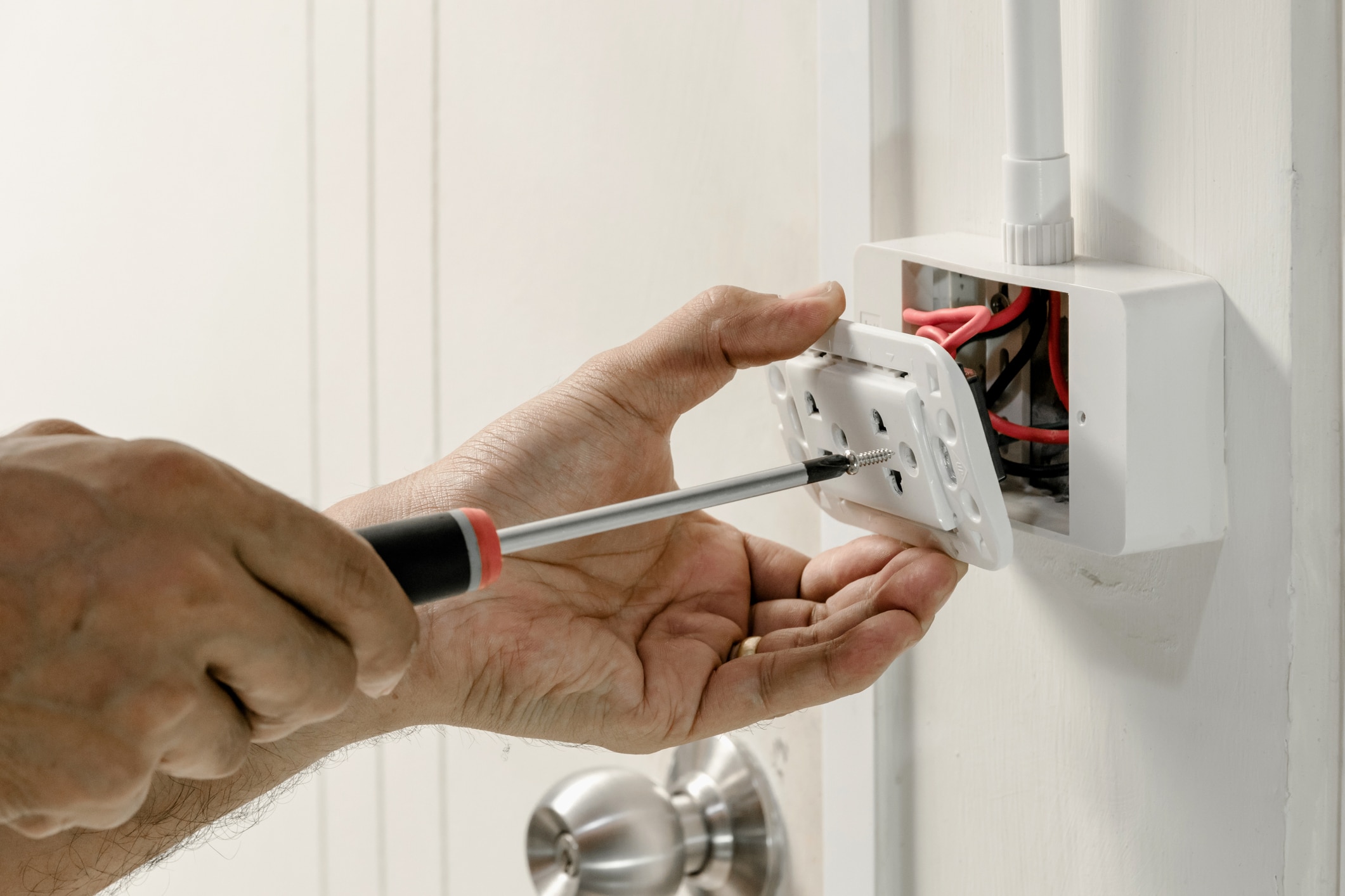 The electrician is using a screwdriver to attach the power cord to the wall outlet