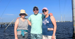 Three smiling people standing in front of a lake