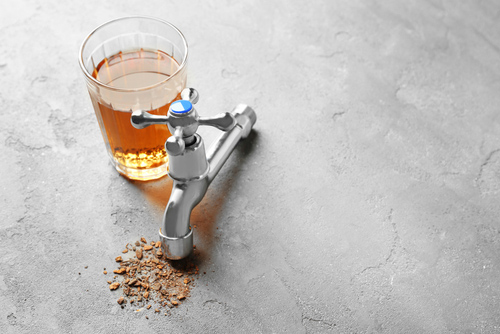 brown water in a glass next to a faucet and a mineral deposit