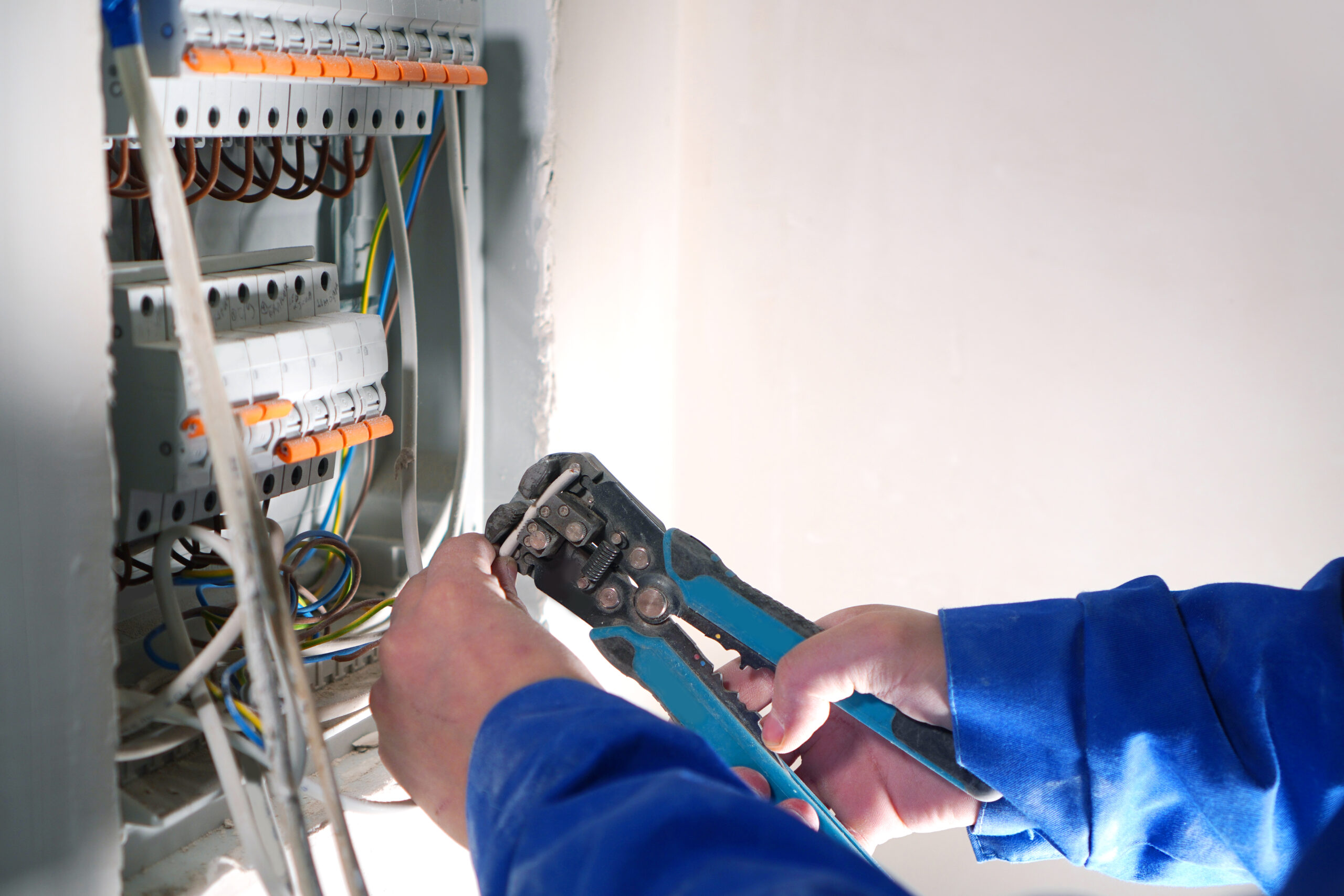 Electrician works on electrical switchboard with automats and wires