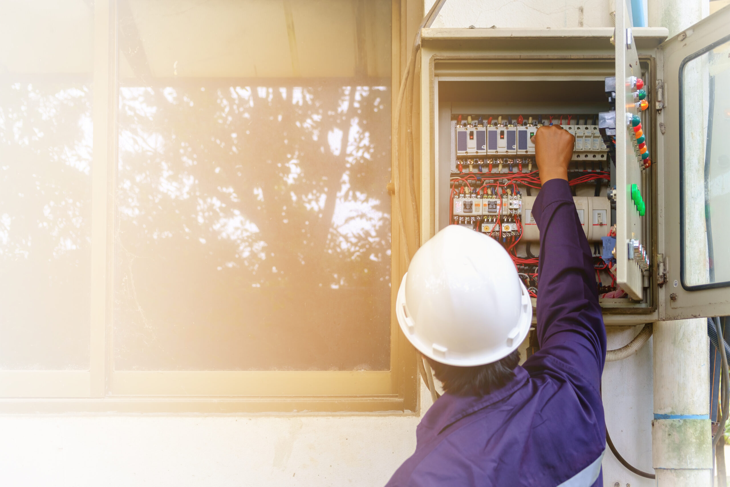 Back of technician in safety uniform and white security helmet turning on switch in the electrical cabinet 