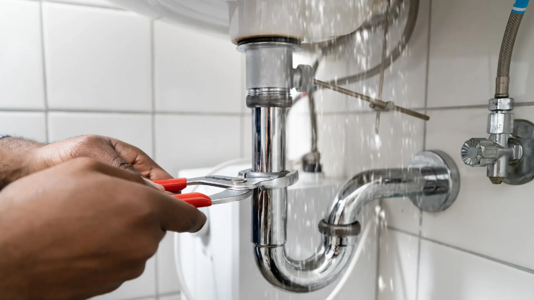 Hands repairing a sink drain trap with pliers